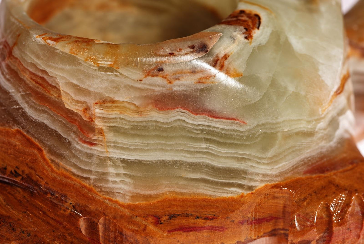 A close-up of a carved onyx candle holder showing layered white, cream and brown stone with a dark surface below.