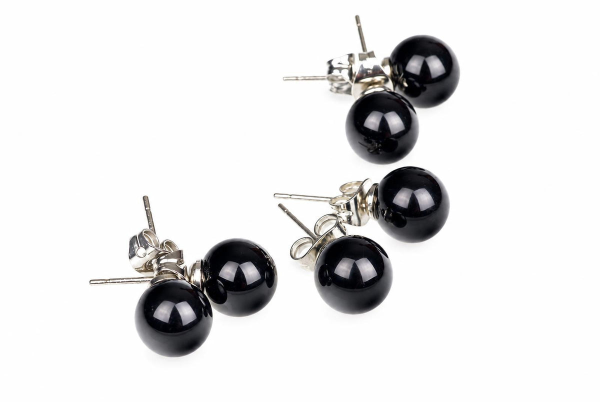 Two pairs of round black stud earrings with silver-toned posts and butterfly backs on a white surface.