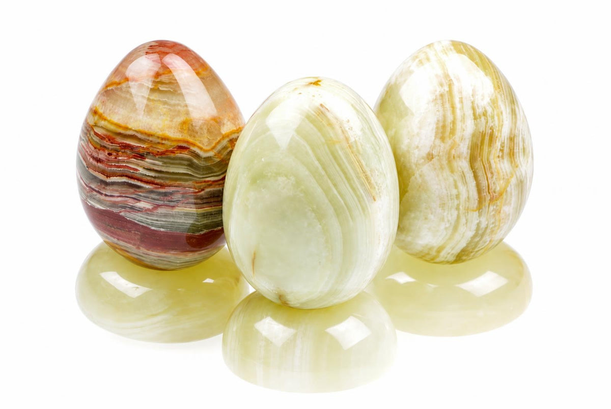 Three polished, egg-shaped stones with layered bands of red, green, white and yellow on a pale reflective surface.