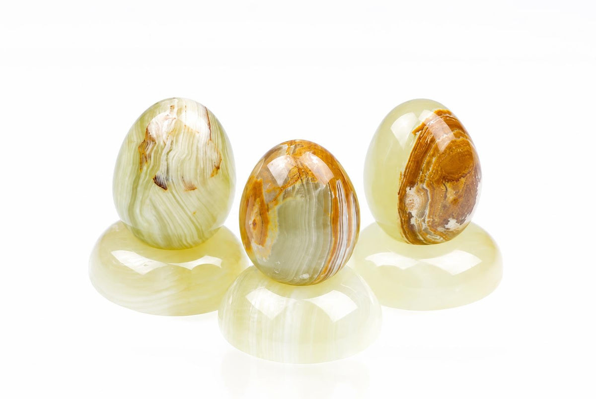 Three polished, egg-shaped stones with green and brown banding stand on matching bases against a white background.