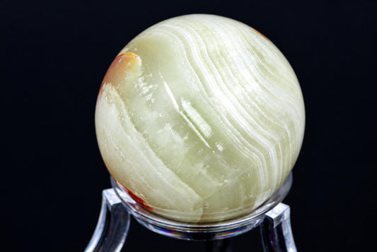 A polished, pale green sphere with white and brown stripes sits on a clear stand against a dark background.