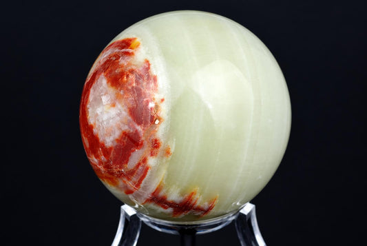 A polished, pale green sphere with red and white patches sits on a clear stand against a dark background.