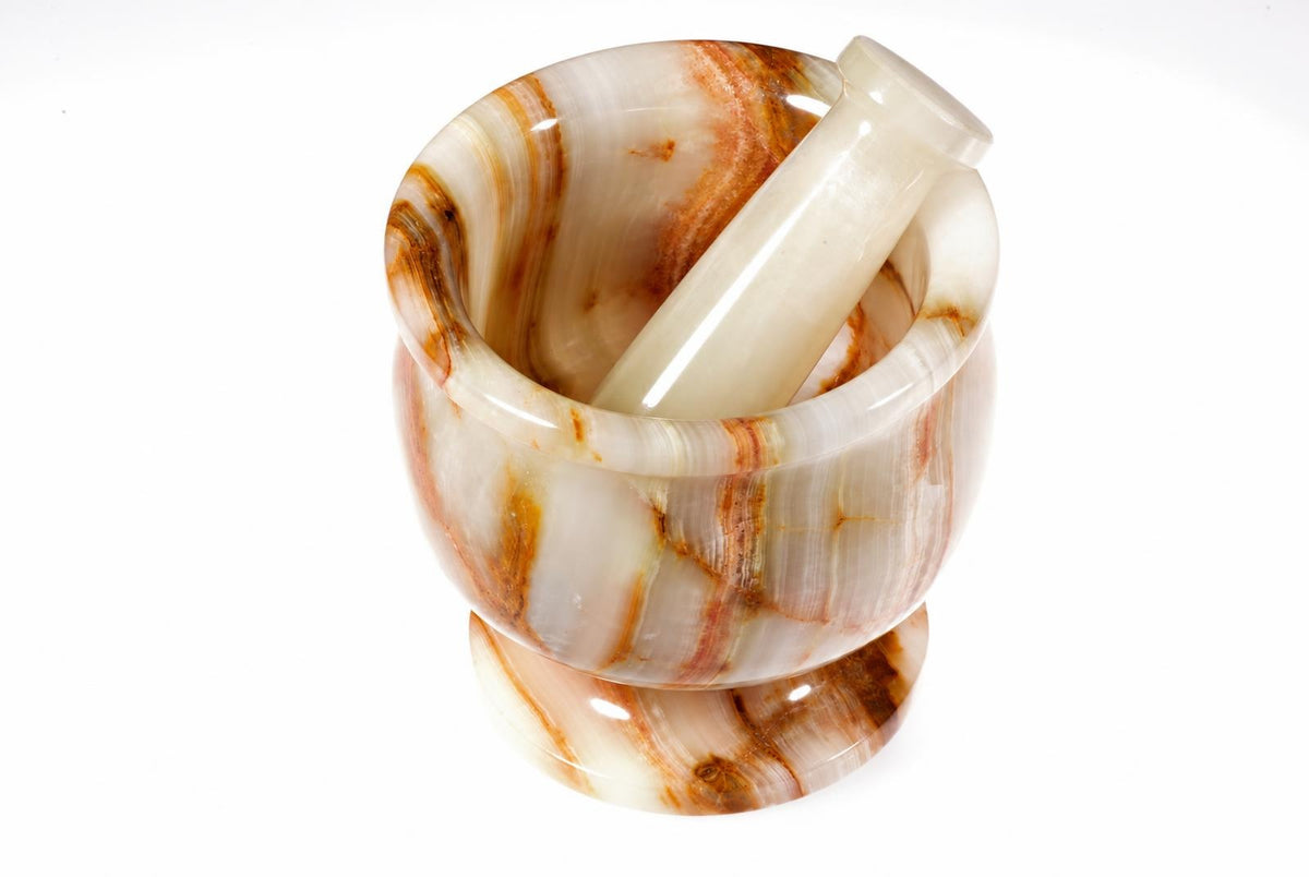 A polished mortar and pestle set with a white base and brown swirls, resting on a pale surface.