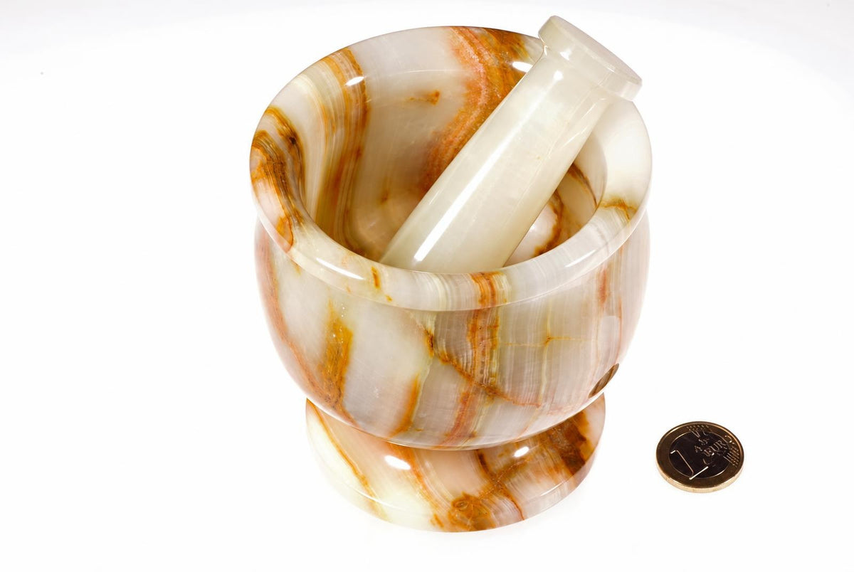 A polished mortar and pestle with white, brown, and orange swirls sits on a pale surface next to a coin.