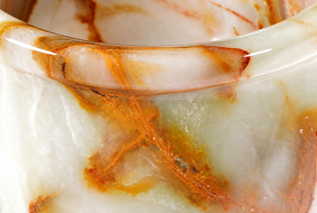 A close-up of a polished, curved onyx object with white, green and orange-brown marbled patterns.