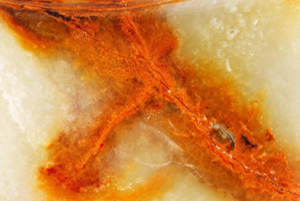A close-up of a polished stone surface with swirling patterns of orange, brown, and pale cream.