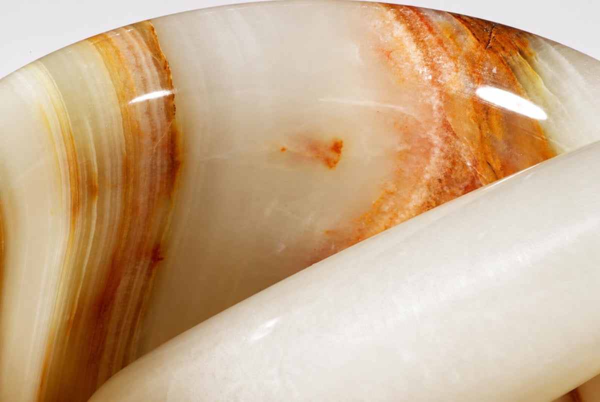 A close-up of a polished onyx hand grinder with curved white and brown stripes, resting on a pale surface.