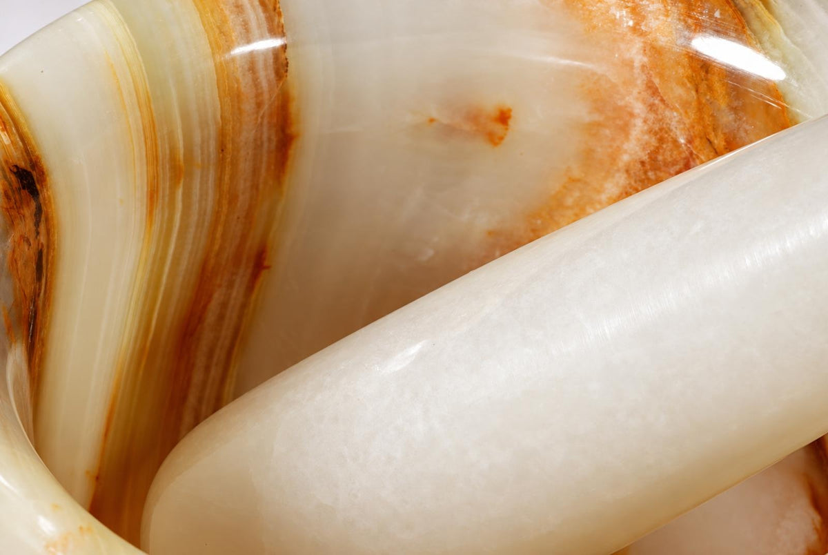A close-up of a white and brown striped onyx hand grinder with a smooth, polished surface.