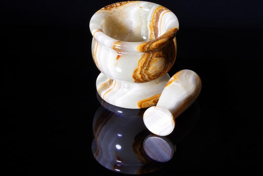 A polished mortar and pestle set with white and brown banded stone, resting on a dark reflective surface.