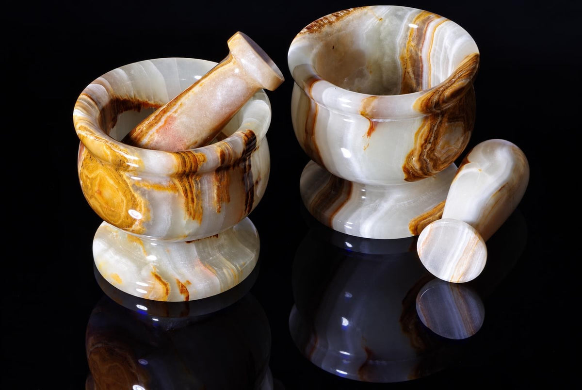 Two pale stone mortars with brown and gold-colored bands are displayed with matching pestles on a reflective black surface.