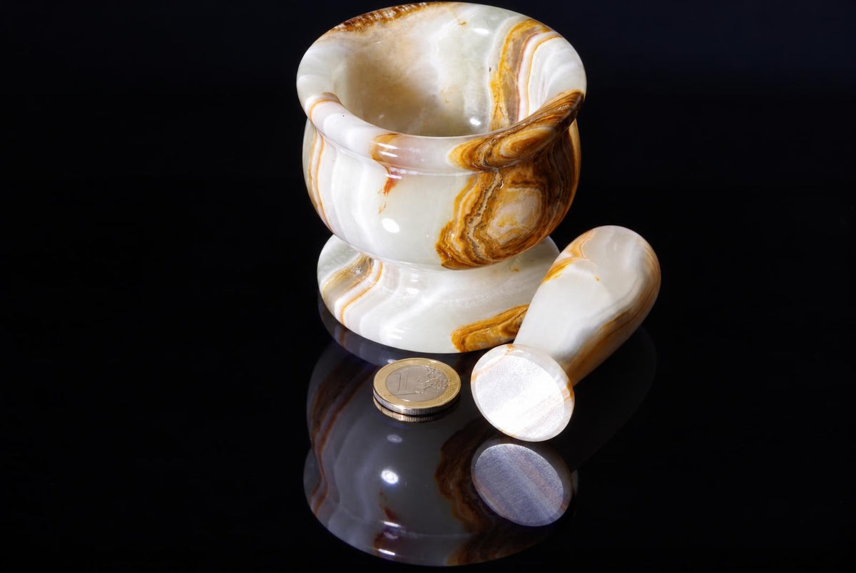 A polished white and brown banded stone mortar and pestle set on a dark reflective surface with a coin for scale.