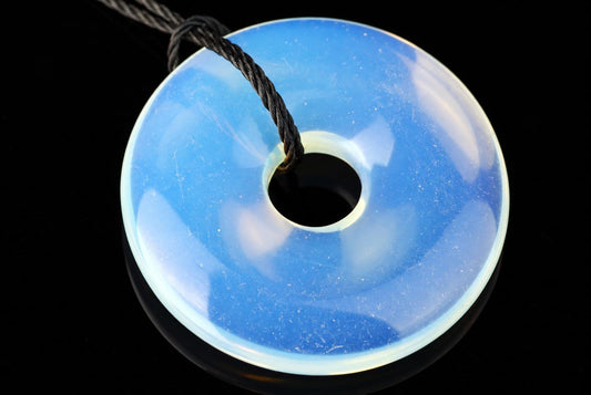 A blue, translucent donut-shaped pendant with a central hole and a black cord looped through it on a dark surface.