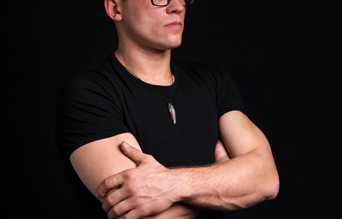 A man in a black t-shirt wears a pendant shaped like an Orthoceras fossil on a dark surface.