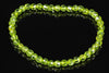 A bracelet of faceted, light green beads arranged in a circle on a dark, reflective surface.