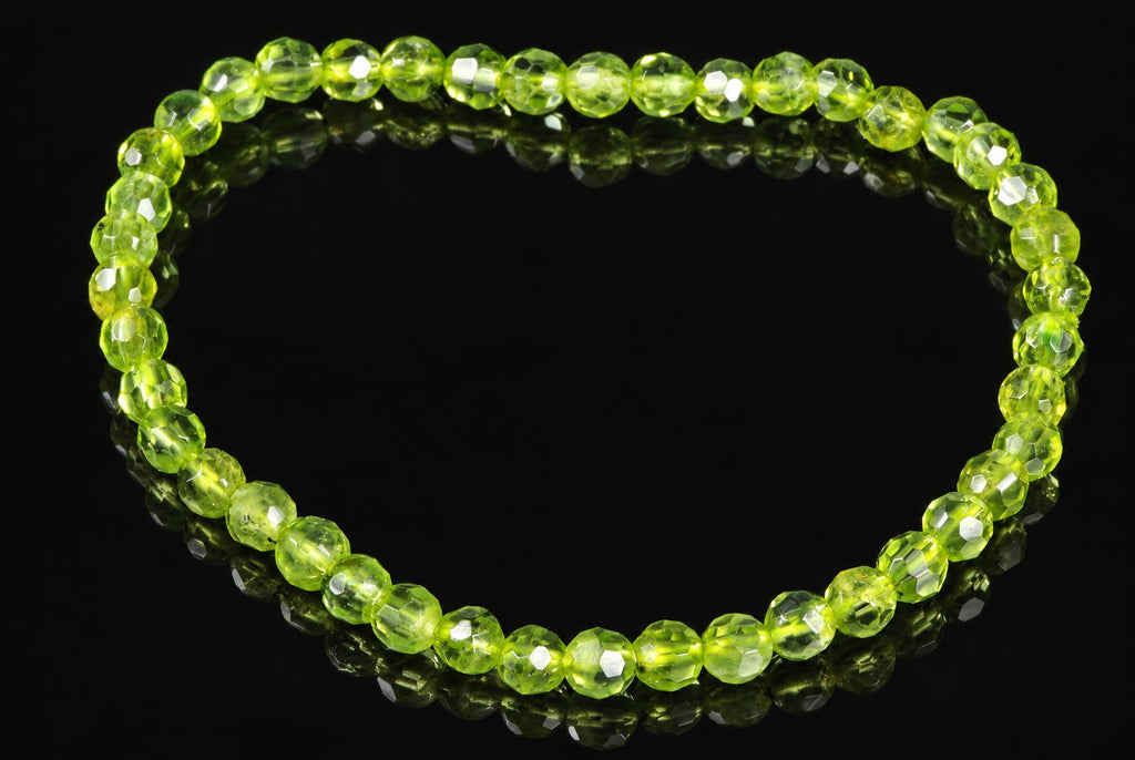 A bracelet of faceted, light green beads arranged in a circle on a dark, reflective surface.