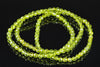 A strand of faceted, lime-green beads arranged in a loose coil on a dark, reflective surface.