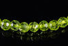 A row of faceted, lime-green beads on a dark reflective surface.