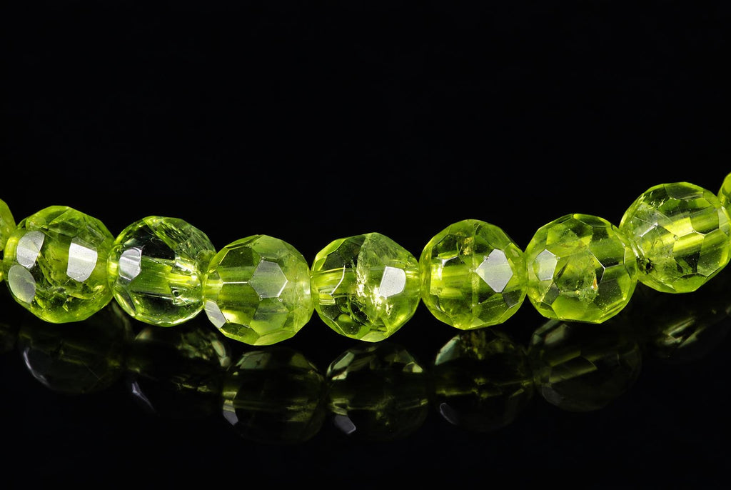 A row of faceted, lime-green beads on a dark reflective surface.
