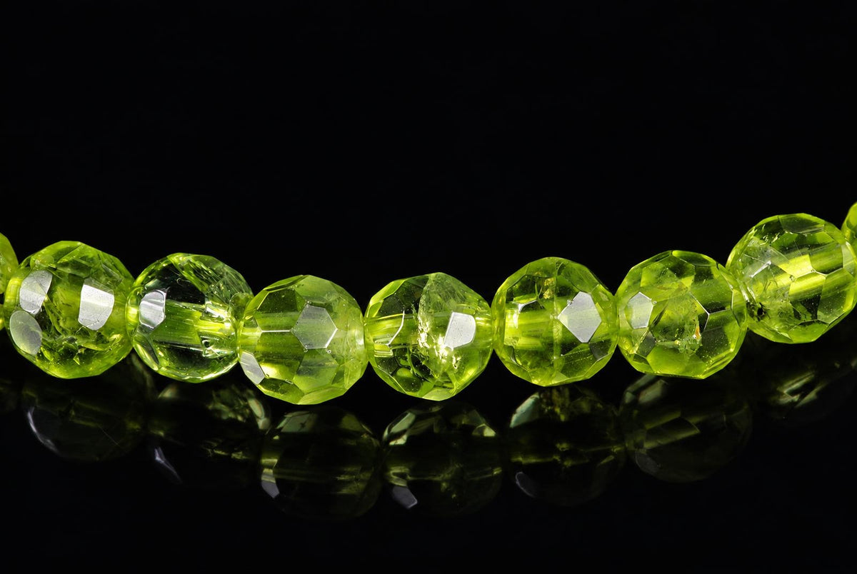 A row of faceted, lime-green beads on a dark reflective surface.