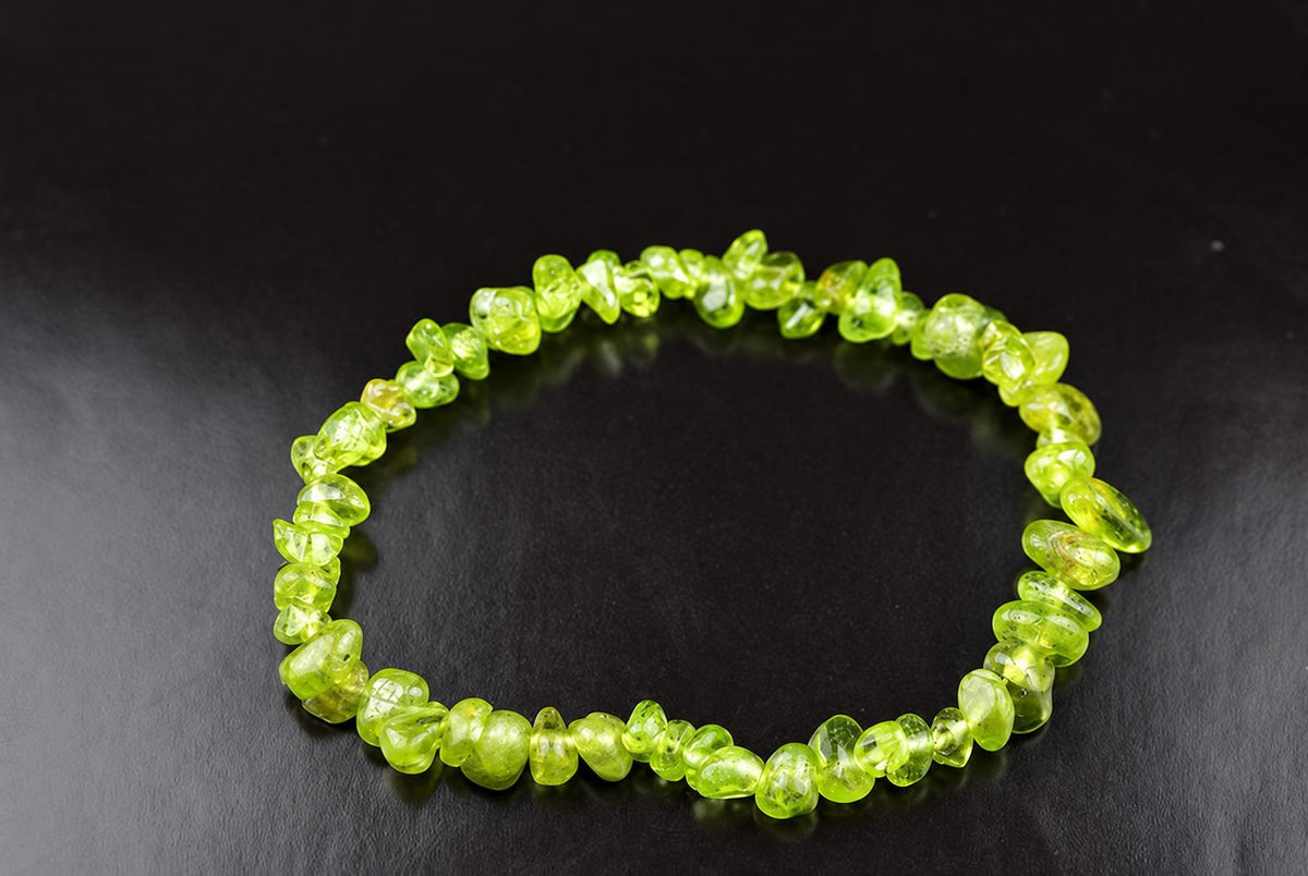 A bracelet of irregular, translucent lime-green chips arranged in a circle on a dark surface.