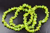 A strand of bright green peridot chip beads arranged in a loose coil on a dark surface.
