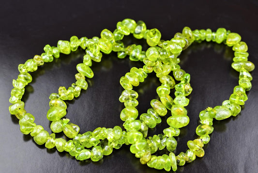 A strand of bright green peridot chip beads arranged in a loose coil on a dark surface.