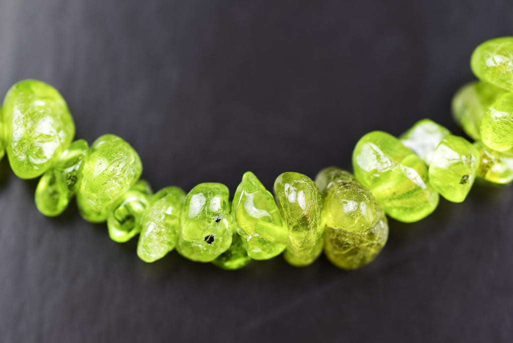 A strand of bright green, translucent peridot chips arranged in a curved line on a dark surface.