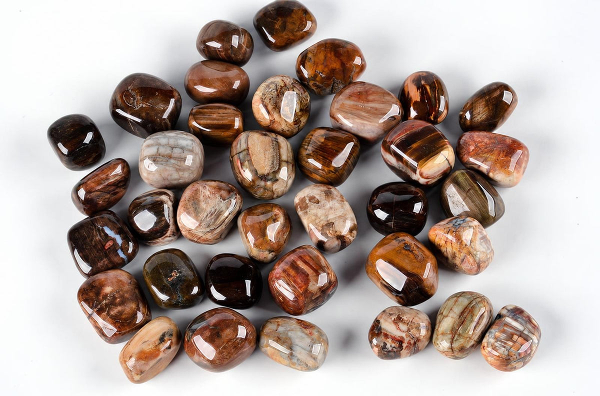 A pile of polished, tumbled stones with brown, tan and grey banding on a white surface.