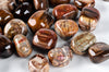 A collection of polished, smooth stones with brown, tan and grey banding patterns on a pale surface.