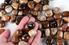 A hand holds polished, rounded stones with brown, black and cream stripes on a pale surface.