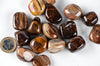 A collection of polished, brown and tan striped stones on a white surface with a Euro coin for scale.