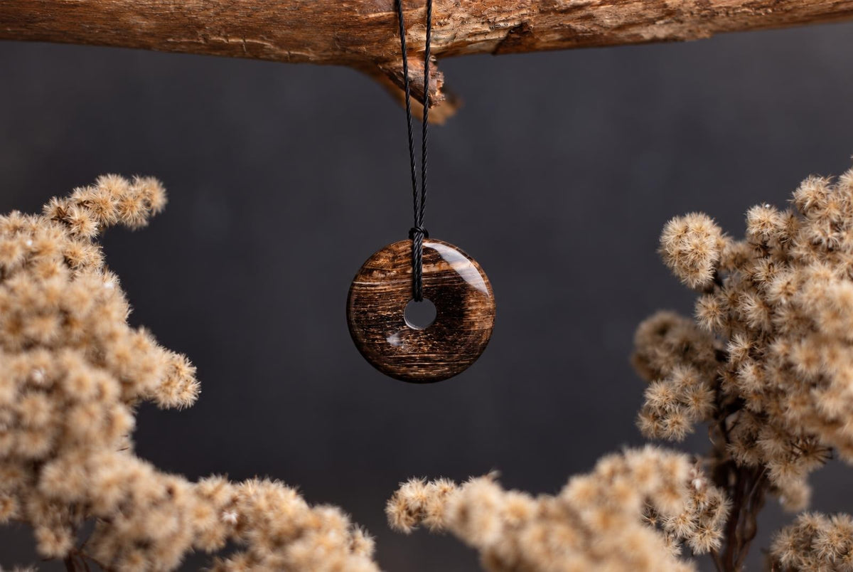 A polished, brown donut-shaped pendant with a central hole hangs from a black cord against a dark background.