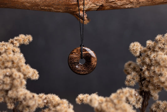 A polished, brown donut-shaped pendant with a central hole hangs from a black cord against a dark background.