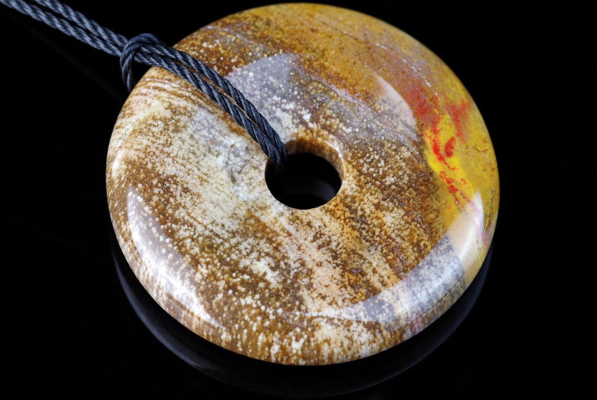 A polished, donut-shaped pendant with a central hole, featuring mottled brown, yellow, and white patterns on a dark surface.