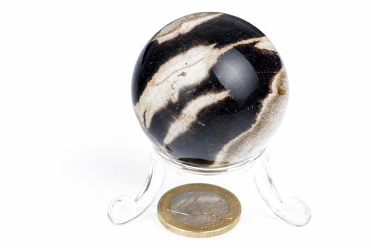 A polished sphere with black and white swirling patterns sits on a clear stand against a white background, next to a coin.