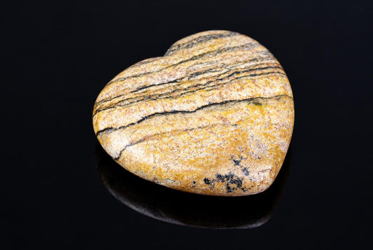 A heart-shaped stone with yellow, white and black stripes rests on a dark reflective surface.