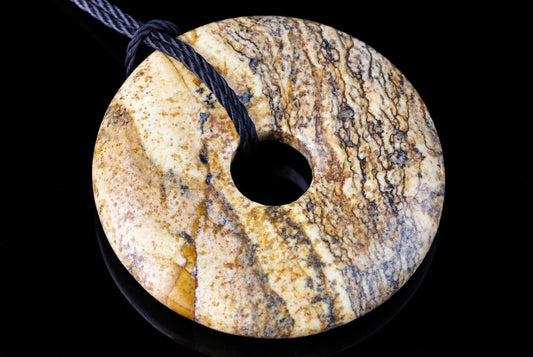 A round, donut-shaped pendant with a central hole, featuring yellow, brown and grey marbled patterns on a dark surface.