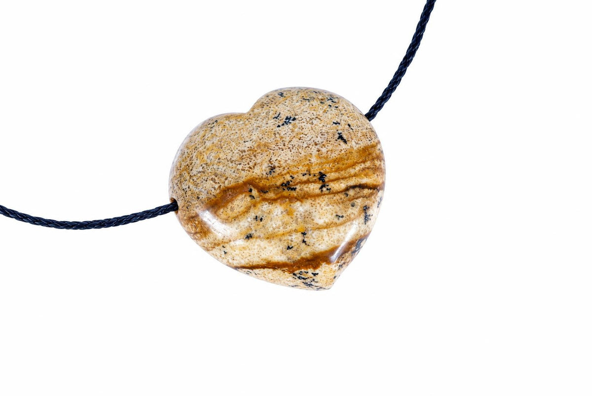 A heart-shaped pendant made of speckled brown and cream stone with dark flecks, threaded on a dark cord against a white background.