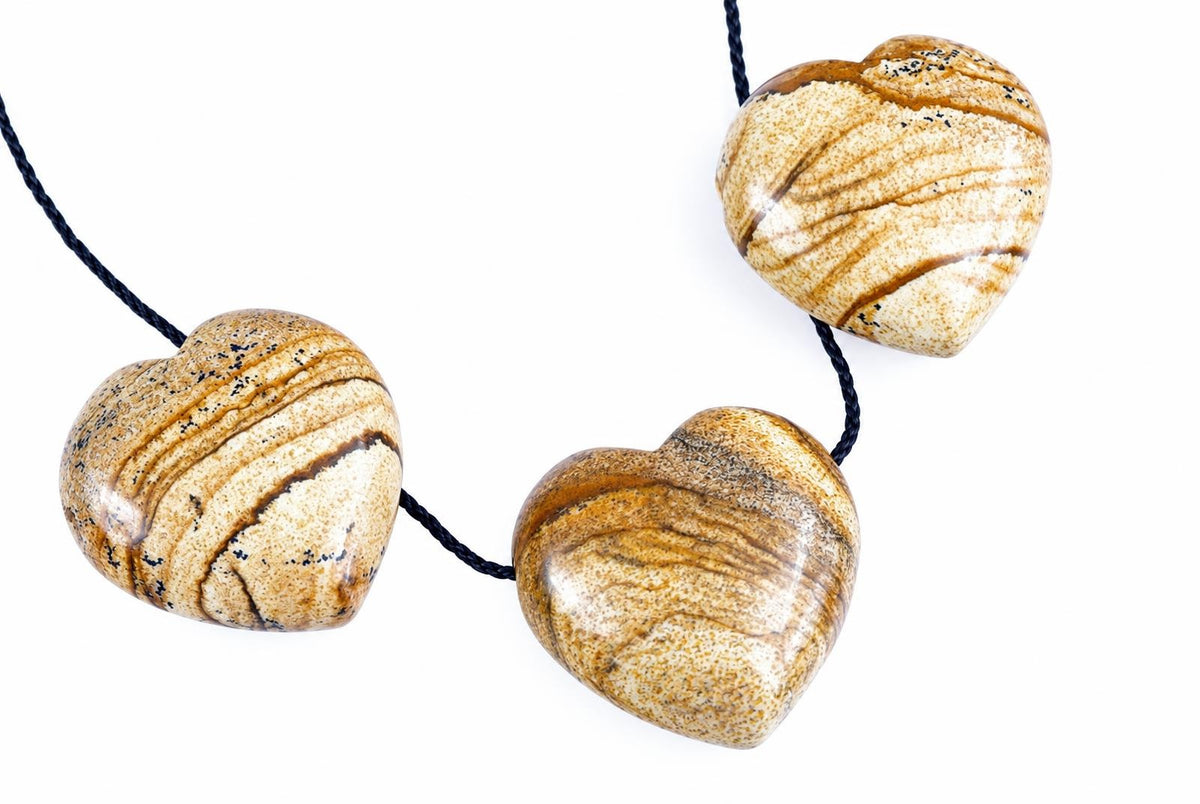 Three polished heart-shaped jasper pendants with brown and cream stripes on a dark cord against a white background.
