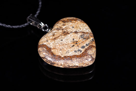 A heart-shaped jasper pendant with brown, black and cream patterns hangs from a silver-toned bail on a dark surface.