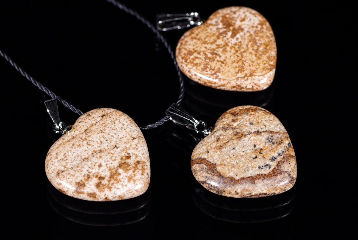 Three heart-shaped jasper pendants with brown and beige speckled patterns hang on dark cords against a black reflective surface.
