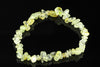 A bracelet made of irregular, polished chips in pale yellow and green tones, arranged on a dark reflective surface.