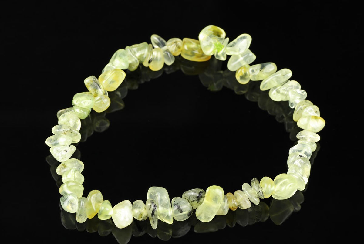 A bracelet made of irregular, polished chips in pale yellow and green tones, arranged on a dark reflective surface.