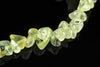 A strand of translucent yellow-green prehnite chips with dark inclusions, arranged on a dark reflective surface.