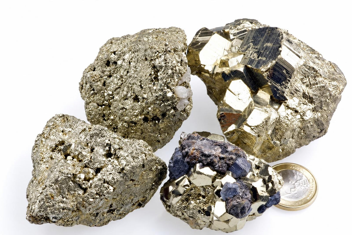 Four metallic gold-toned mineral clusters with angular faces and dark patches rest beside a coin on white.