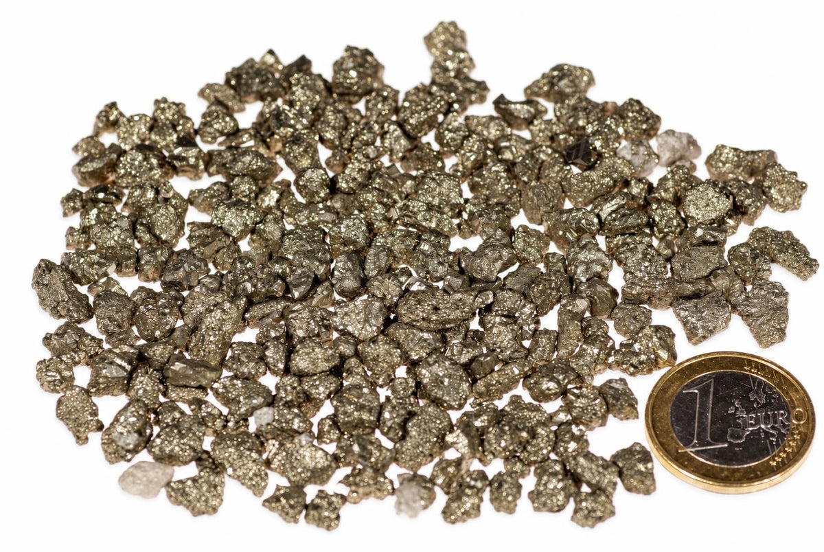 A pile of small, metallic gold-coloured pyrite crystals on a white surface next to a one euro coin.