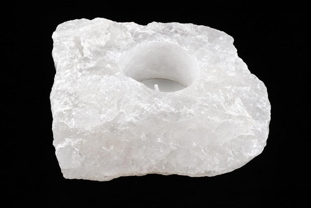 A rough white stone candle holder with a round central recess and a tealight is shown against a black background.