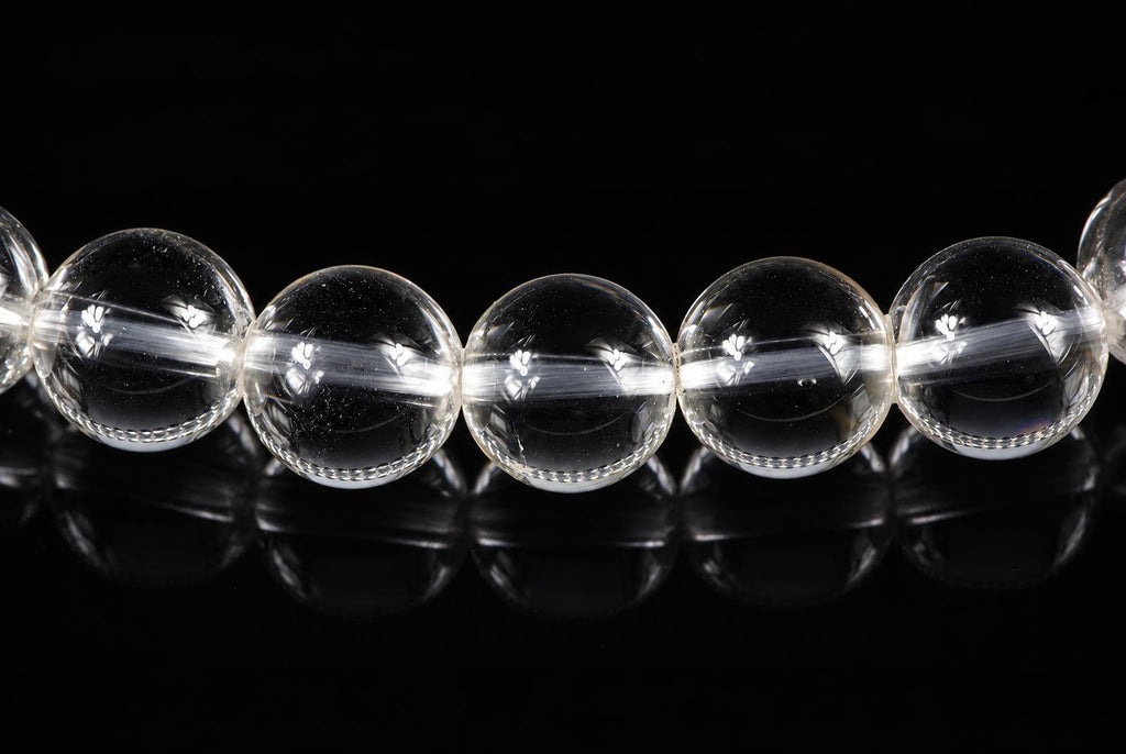 A row of clear, round quartz beads with internal inclusions on a dark reflective surface.