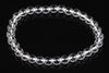 A bracelet of clear, round quartz beads on a dark reflective surface.