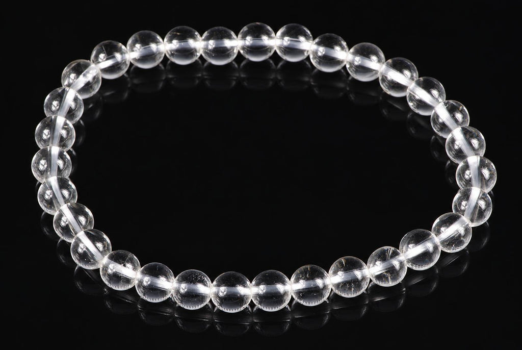 A bracelet of clear, round quartz beads on a dark reflective surface.